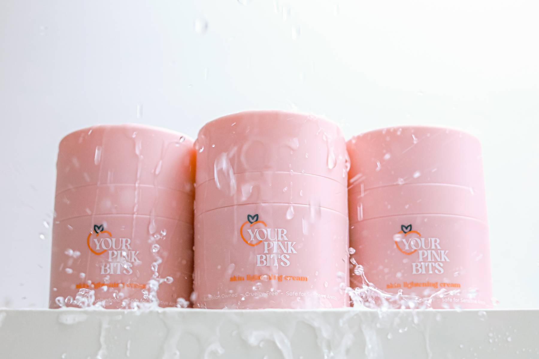 Three YPB Skin Tone Correcting & Brightening Cream containers with water pouring over.